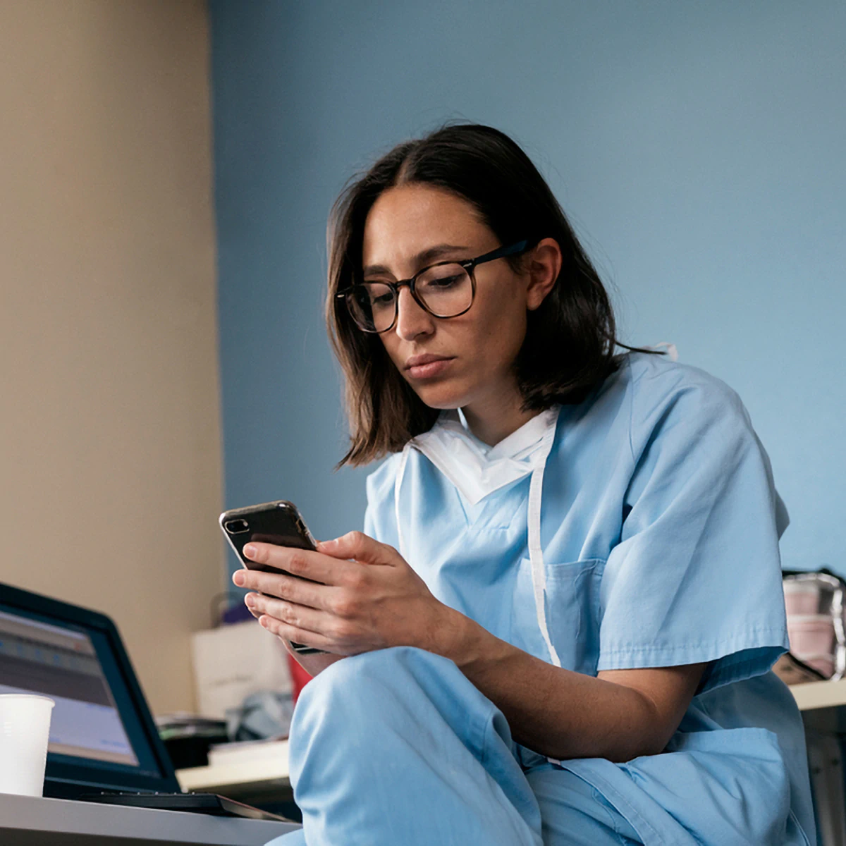 A doctor in scrubs uses their phone to explore earning opportunities on Sermo